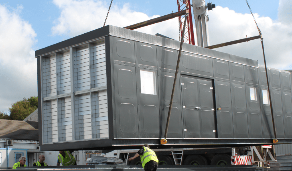 A grey bespoke designed Acoustic Container being crane lifted into place by Mansfield Pollard on-site installers.